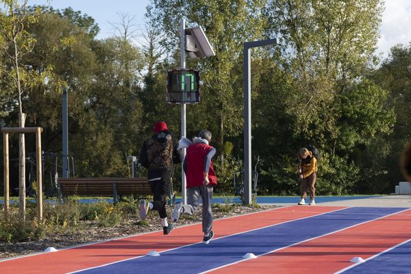 Zwei Läufer auf der Leichtathletikbahn in Saint-Dizier mit einer EVOLIS Vision Geschwindigkeitsanzeigetafel, die eine Geschwindigkeit von 17 km/h anzeigt.